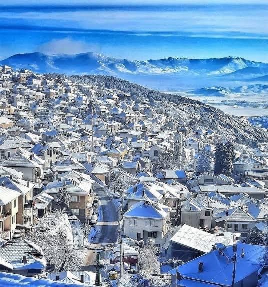 The town of Krushevo covered in snow, with clear blue skies and snow-filled mountains in the background. 